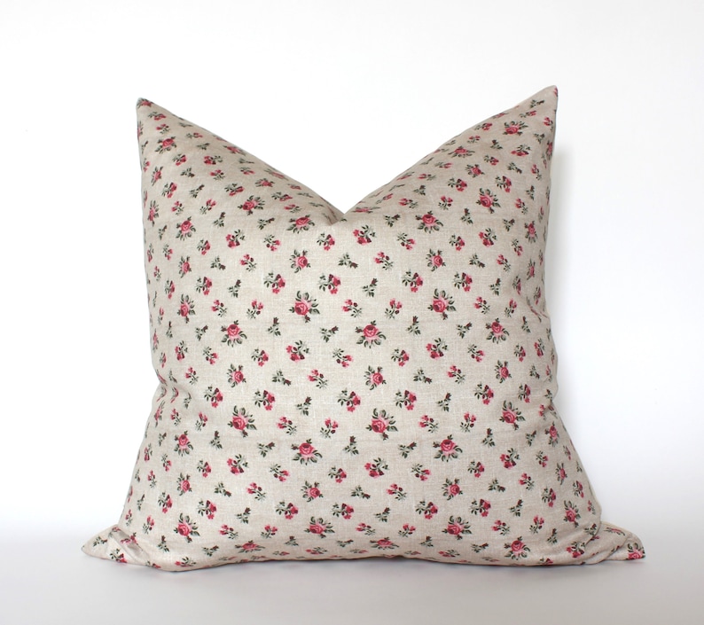 May include: A beige pillow with a small pink rose pattern. The pillow is made of a soft, linen-like fabric.