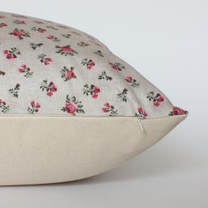 May include: A beige pillow with a zipper closure. The pillow cover features a small-scale floral pattern with pink roses and green leaves.