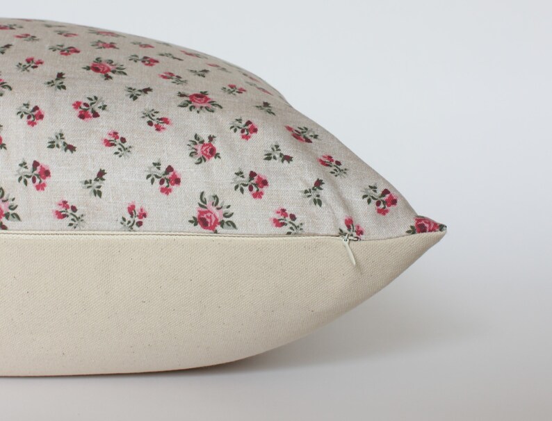 May include: A beige pillow with a zipper closure. The pillow cover features a small-scale floral pattern with pink roses and green leaves.