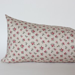 May include: A long, rectangular pillow with a beige linen fabric cover featuring a small-scale floral pattern of pink roses and green leaves.