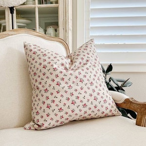 May include: A white chair with a floral patterned pillow. The pillow has a small pink floral pattern on a white background.