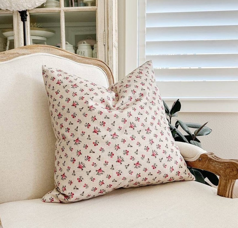 May include: A white chair with a floral patterned pillow. The pillow has a small pink floral pattern on a white background.