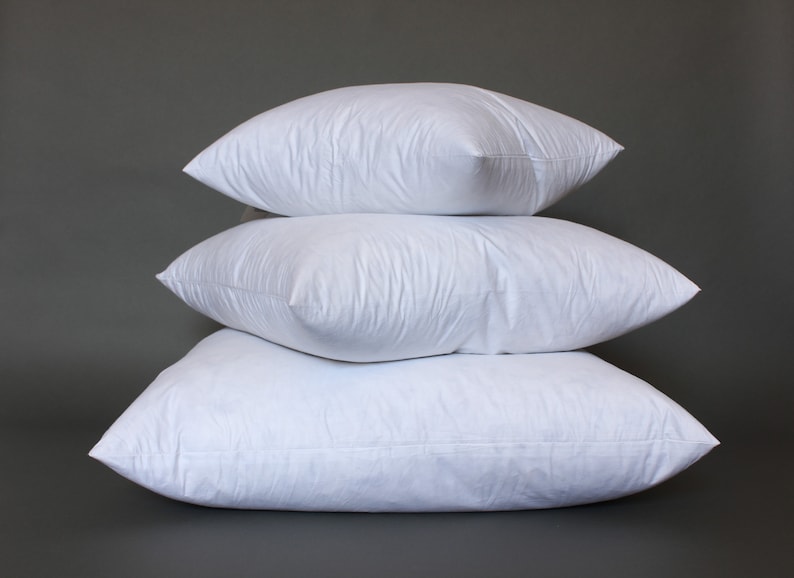Puede incluir: Tres almohadas blancas apiladas una encima de la otra sobre un fondo gris.