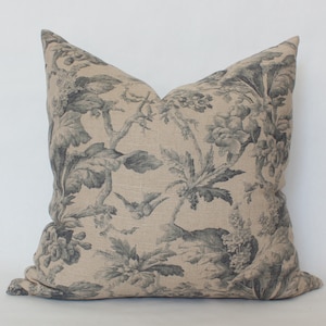 May include: A decorative throw pillow with a beige linen fabric and a black and white floral pattern. The pillow features a repeating pattern of stylised flowers, leaves, and birds.