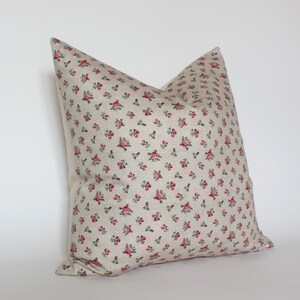 May include: A beige pillow with a small pink floral pattern. The pillow is made of a soft, textured fabric.