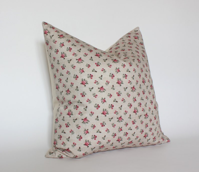 May include: A beige pillow with a small pink floral pattern. The pillow is made of a soft, textured fabric.