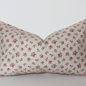 May include: A beige pillow with a small pink floral pattern. The pillow is made of a soft, linen-like fabric.