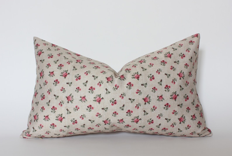 May include: A beige pillow with a small pink floral pattern. The pillow is made of a soft, linen-like fabric.