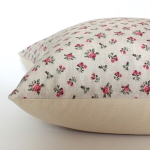 May include: A beige pillow with a floral pattern featuring small pink roses. The pillow has a plain beige border.