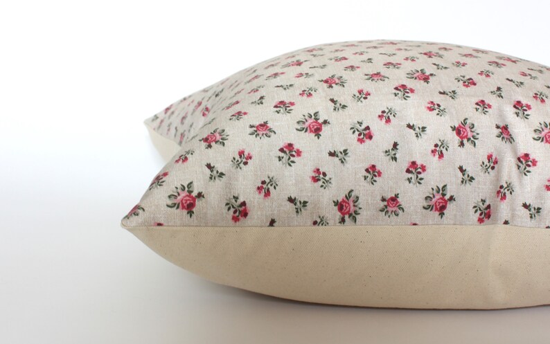 May include: A beige pillow with a floral pattern featuring small pink roses. The pillow has a plain beige border.