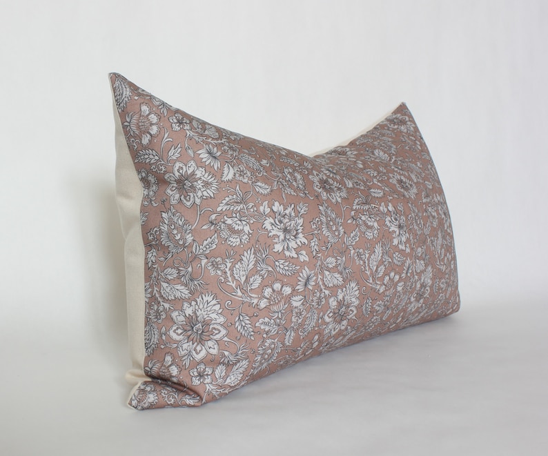 May include: A rectangular pillow with a floral pattern in shades of pink and white. The pillow has a white border and is made of a soft, comfortable fabric.