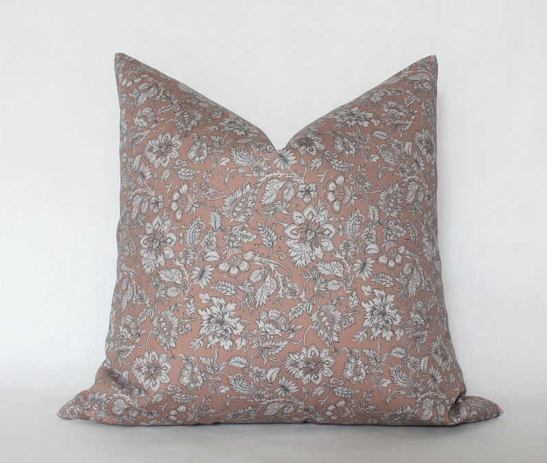 May include: A blush pink pillow with a white floral pattern. The pillow is made of a soft, comfortable fabric and has a subtle sheen.