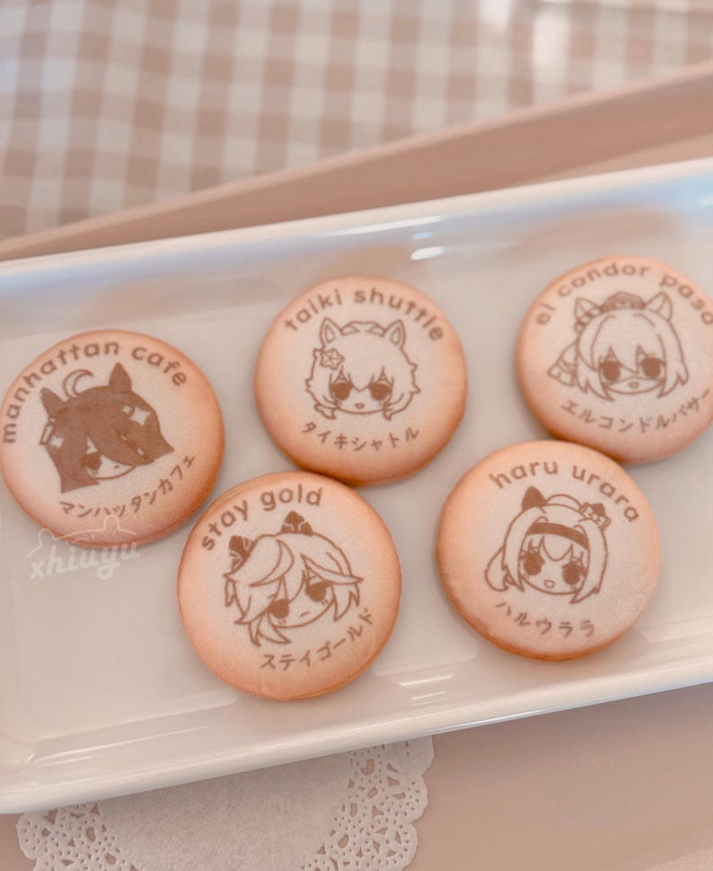 May include: Six round cookies with cartoon character illustrations and Japanese text. The cookies are light brown with brown illustrations and text. The cookies are arranged on a white rectangular plate.