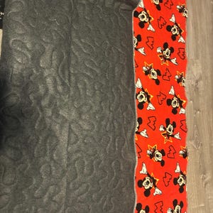 May include: A section of a quilt with a gray, patterned fabric on the left and a red fabric with a Mickey Mouse print on the right. The Mickey Mouse fabric has a white border.