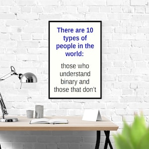 May include: A black framed poster with white text that reads "There are 10 types of people in the world: those who understand binary and those that don't". The poster is hanging on a white brick wall above a wooden desk with a silver lamp, two cups, and a book.