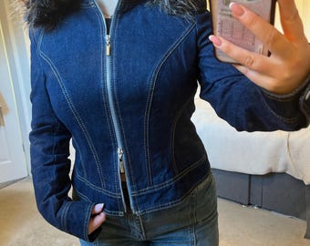 May include: A dark blue denim jacket with a faux fur collar. The jacket features a silver zipper and light-colored stitching. The jacket is fitted and has a classic design.