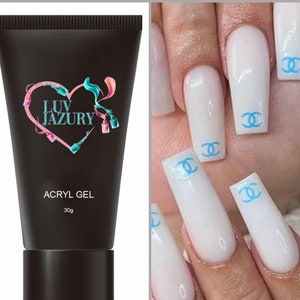 May include: A black tube of acrylic gel with the brand name "Luv Jazury" and a pink heart logo. The tube is labelled "ACRYL GEL" and "30g". The image also shows a hand with white nails decorated with blue Chanel logos.