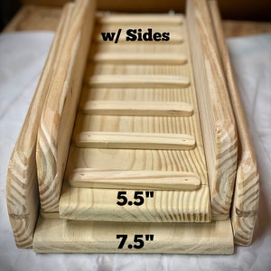 Placed on a white cloth, these pressure treated ramps  with sides are stacked from largest to smallest starting with a 7.5 inch wide ramp 5.5 inch wide ramp they both have rungs spaced 3 inches apart and are sanded smooth  the sides are 2.5 inches