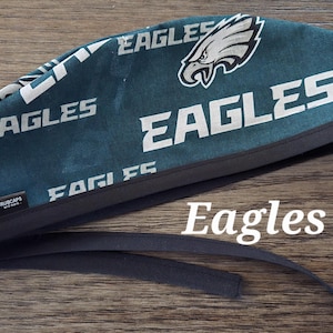 May include: Green and white scrub cap with the word "Eagles" repeated on the fabric. The cap has a black elastic band.