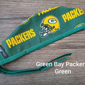 May include: Green and yellow Green Bay Packers surgical scrub hat with a green and white football helmet graphic. The hat has a green tie.