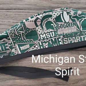 Peut inclure: Un bonnet de gommage à motifs verts et blancs avec le texte "MSU HOME SPARTANS" et "GO GREEN GO WHITE". Le bonnet a une bordure et des liens noirs. Les mots "Michigan State Spirit" sont également visibles.