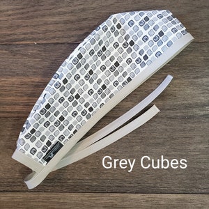 May include: Grey and white patterned surgical scrub cap with a grey tie. The pattern is small grey squares on a white background. The text "Grey Cubes" is printed below the cap.