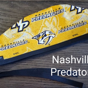 May include: A yellow and black headband with the Nashville Predators logo and the text "Nashville Predators" repeated on the fabric. The headband has a black elastic band.