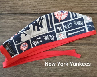 May include: Red and blue patterned surgical scrub hat with a red tie. The pattern features the New York Yankees logo, baseball bats, and baseballs. The hat is labeled "New York Yankees".