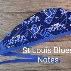 May include: Blue and white surgical scrub hat with a repeating pattern of the St. Louis Blues NHL hockey team logo. The hat has a blue elastic band.