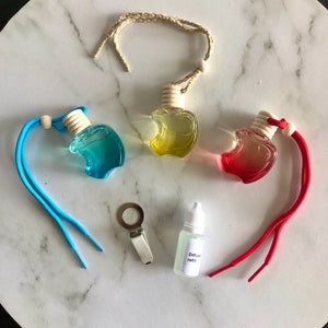 May include: Three apple-shaped car air fresheners with blue, yellow, and red liquid. Each air freshener has a string for hanging. A small bottle of diffuser refill and a metal clip are also included.