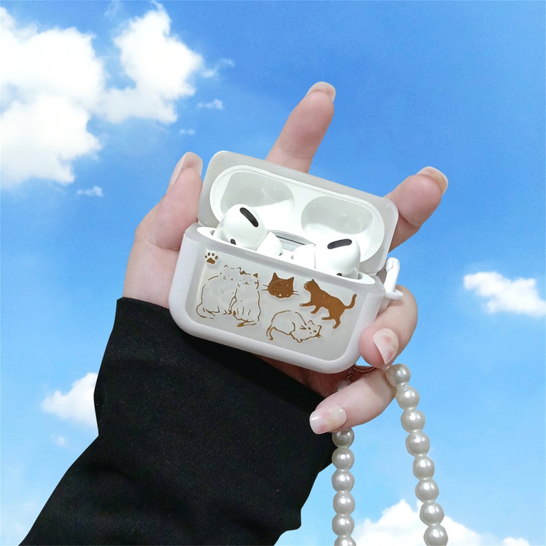 May include: White Airpods case with a gold cat design and a white pearl necklace attached.