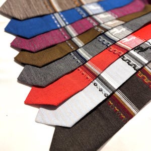 Peut inclure: Une collection de cravates disposées en éventail, présentant diverses couleurs dont le marron, le bleu, le magenta, le gris, le rouge et le blanc. Les cravates affichent des textures variées, des motifs tissés et des détails rayés.