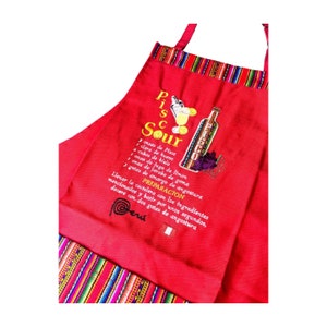 May include: Red kitchen apron with a colourful striped border. The apron features an embroidered design of a Pisco Sour cocktail recipe in Spanish with a glass of the drink and a bottle of Pisco.