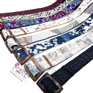 May include: A collection of colorful fabric belts with unique patterns and designs. The belts are handmade in Peru and feature wooden buckles. The text on the tag reads "Original Peruvian Craft Handmade in Peru".