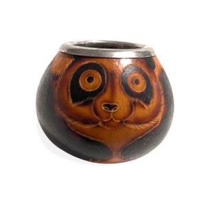 Peut inclure: Une gourde brune avec un bord en métal argenté, ornée d'un motif de visage de panda peint à la main. Le panda a des yeux noirs, un nez noir et des oreilles noires.