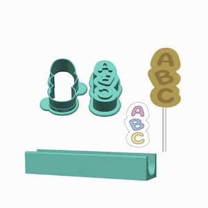 Può includere: Un set di tagliabiscotti in plastica color verde acqua con le lettere A, B e C impilate verticalmente. Il set include un supporto rettangolare abbinato, un piccolo adesivo con le lettere A, B, C e una sagoma a forma di lecca-lecca.