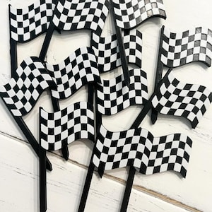 May include: A group of black and white chequered racing flags on black sticks. The flags are waving, and the image is taken from above. The flags are arranged on a white wooden surface.