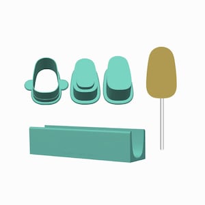 Può includere: Un set di strumenti in plastica color verde acqua che include un supporto rettangolare con canale a U, due taglierine ovali, una taglierina ovale aperta con linguette laterali e una paletta ovale color marrone chiaro su un bastoncino bianco.