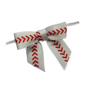 May include: A white ribbon bow with red stitching, resembling a baseball. The bow features a series of red chevrons along the edges, mimicking the seams of a baseball. The bow is tied with a clear plastic tie.