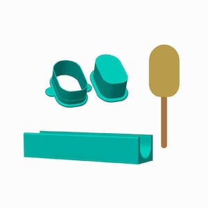May include: A set of teal baking tools including an oval cutter, a solid oval plunger, a long rectangular tray with a semi-circular cutout, and a tan popsicle-shaped tool with a thin brown handle, all arranged against a plain white background.