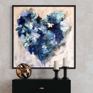 May include: A black framed painting of a blue and white abstract heart-shaped floral design hangs above a black two-drawer dresser with gold knobs. A gold metal sphere sits on the dresser, and two candlesticks with white candles are on either side of the sphere.