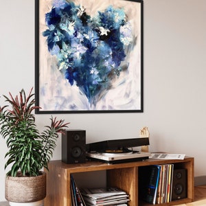 May include: A framed abstract painting of a blue heart-shaped design on a white background. The painting is hanging on a white wall above a wooden shelf with a record player, speakers, and records.