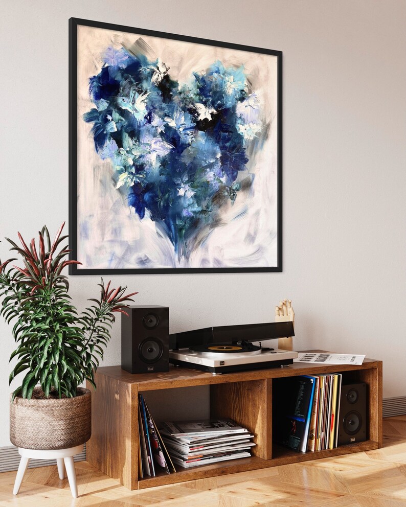May include: A framed abstract painting of a blue heart-shaped design on a white background. The painting is hanging on a white wall above a wooden shelf with a record player, speakers, and records.