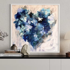 May include: Abstract painting of a blue heart-shaped floral arrangement on a white background. The painting is framed in a white frame and is hanging on a white wall.