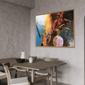Op de afbeelding: Abstracte schilderij van muziekinstrumenten, waaronder een saxofoon, een viool en een drumstel, in tinten blauw, oranje, geel en bruin. Het schilderij is ingelijst in een houten lijst en hangt aan een grijze muur.