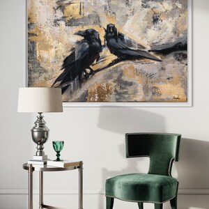 Puede incluir: Pintura abstracta de dos cuervos negros posados en una rama, con un fondo dorado y gris. La pintura est&aacute; enmarcada en un marco blanco.