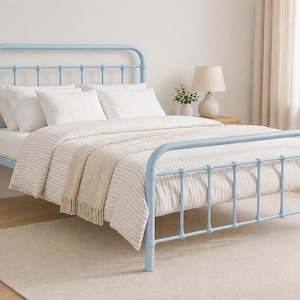 May include: A pale blue metal bed frame with a headboard and footboard. The bed is made up with white bedding and a striped blanket. The room has a neutral rug and a lamp on a bedside table.