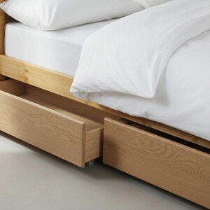 May include: A light-colored wooden bed frame with two pull-out drawers. The bed is made of light-colored wood and has a white mattress and bedding. The drawers are open, revealing the interior space.