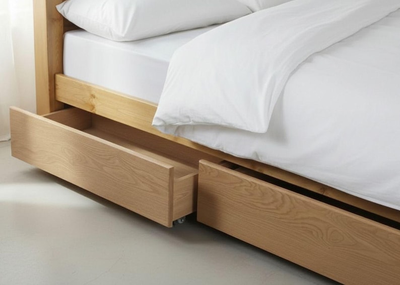 May include: A light-colored wooden bed frame with two pull-out drawers. The bed is made of light-colored wood and has a white mattress and bedding. The drawers are open, revealing the interior space.