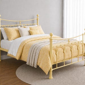 May include: A yellow metal bedstead with a matching headboard and footboard. The bed is made up with yellow patterned bedding, white sheets, and decorative pillows. A light grey throw blanket is draped across the foot of the bed.